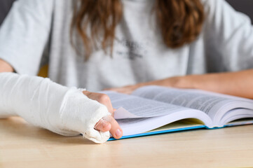 A teenage girl with a hand injury reads a book. Close-up of a bandaged hand on a book. Selective...