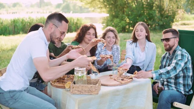 Group of friends are relaxing together outdoor. Young people are sitting at the table, having fun talking and eating pizza.