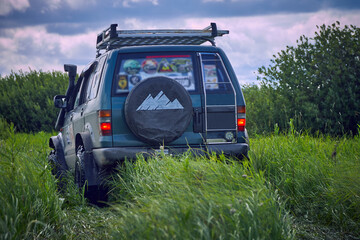 Rear view of a 4x4 SUV in the wild. The off-road car is moving among the lush green grass on the background of beautiful clouds. The concept of travel and adventure © Aleksandr