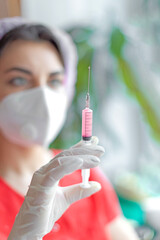 A nurse holds a syringe with an injection in her hands, ready to give an injection. The concept of healthcare and vaccination. The background is blurred