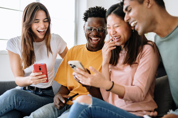 Young group of diverse friends sitting on sofa using mobile phone - Smiling multiracial teenage...