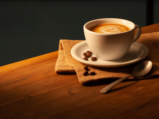 Latte coffee in porcelain cup with napkin and coffee beans on wooden board. Cafe con leche en taza de porcelana con servilleta  y granos de café sobre tabla de madera.
