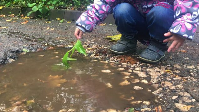 A child plays in a puddle with a green leaf. Rainy weather outdoor games