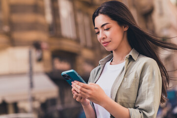 Photo of lovely cute young asian woman wear khaki shirt enjoying sunshine typing modern device outside urban city street