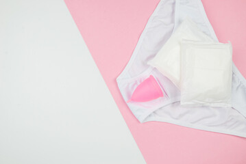 panty pads and menstrual cup on pink and white background with copy space,