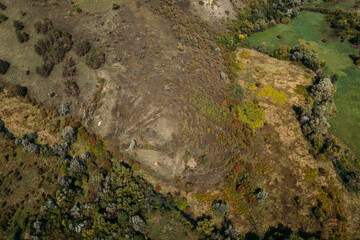 Aerial top view of the green and yellow grass on the autumn hill. Drone shot of a country road.