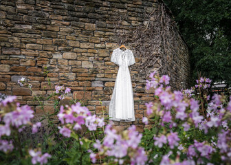 Beautiful wedding dress hanging on stone wall with purple beautiful flowers in foreground