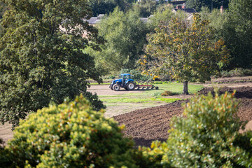 Blue tractor ploughing field out in countryside farm setting for natural crops on summers day