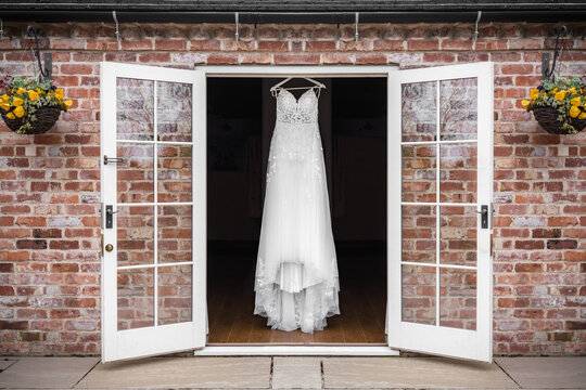 Beautiful White Lace Wedding Dress Hanging In Open Doorway On Summers Day Ready For Bride To Dress And Get Married.