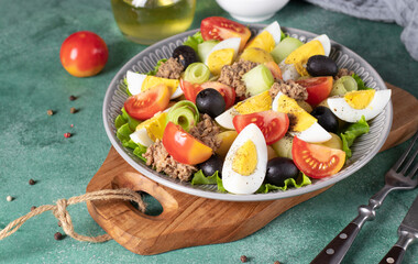 Fototapeta na wymiar French salad Nicoise with canned tuna, boiled potatoes, egg, black olives, cucumbers, tomatoes and lettuce on gray plate on wooden board