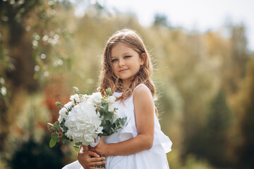 Beautiful girl child with a white dress with a bouquet of flowers, portrait in nature