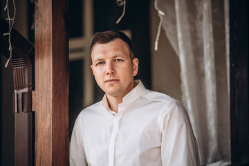 Handsome young adult man in a white shirt, portrait on the terrace of the house