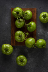 scattered tomatoes, freshly harvested green berries on a textured black table top surface, taken from above