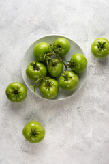 tomatoes on a white plate, freshly harvested green berries scattered on a textured table top surface, taken from above with copy space