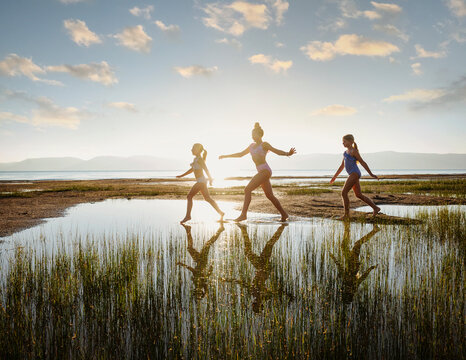 Girls (10-11, 12-13, 14-15) walking on stepping stones in lake at sunrise
