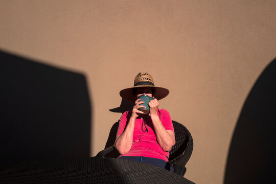 Woman drinking&nbsp;coffee against adobe wall on sunlit patio