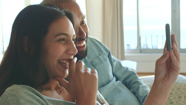 Couple, phone and waving on video call while talking, laughing and greeting people on communication technology in house living room. Smile, happy and comic man and woman with mobile social media chat