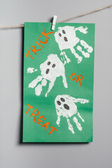 Halloween white ghosts childs handprints drawing on green paper hanging on rope on gray wall. Handmade DIY decoration with children for holiday. Vertical