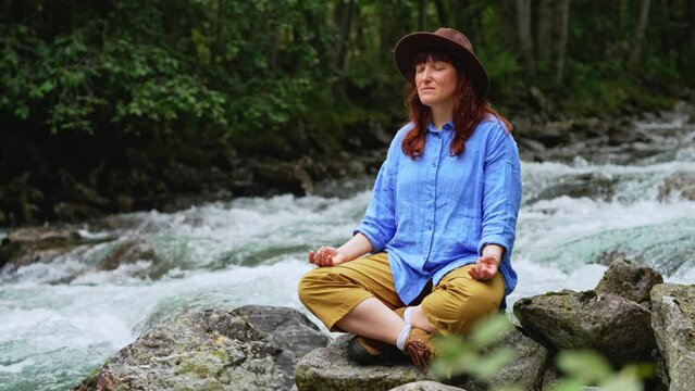 Portrait girl in a hat and blue shirtmeditates near the waterfall and the river in in the spring. Female relax outdoor