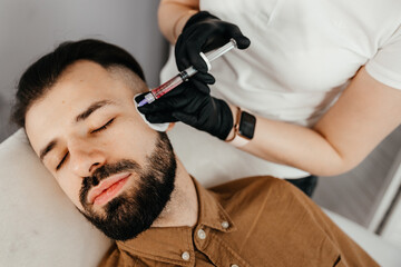 Stylish bearded man visiting aesthetic clinic, getting lips filler, closeup. Man having beauty injection at male spa salon. Anti-aging treatment for men concept