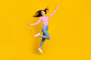 Full length photo of cheerful gorgeous girl wear striped long sleeve jeans arms plane wings flying isolated on yellow color background