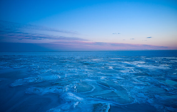 Aerial view of sunset over the frozen sea. Winter landscape on seashore during dusk. View from above of melting ice in ocean on sunrise with horizon. Global warming. Vivid colorful skyline scenics.