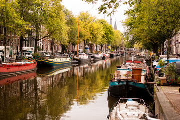 Obraz premium Canal con agua de amsterdam con barcos viviendas edificios calles y árboles, holanda, países bajos.