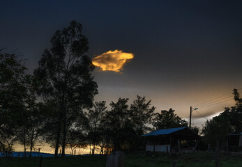 Dusk time yellow cloud on a dark blue sky. Colorful dark sunset landscape with a house and a light post in the countryside © Luis Fernando Acosta