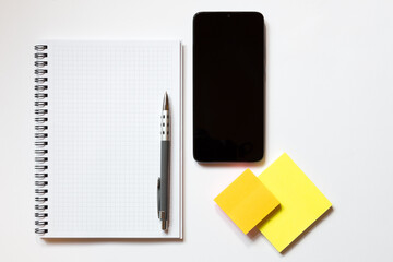 Top down view of notepad with white pages pen smartphone sticky note blocks on white background