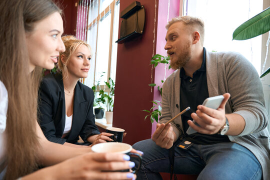Male showing photos on cellphone to colleagues in coworking space