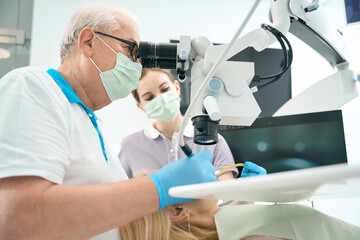 Naklejka na ściany i meble Dentist working with the patient and microscope