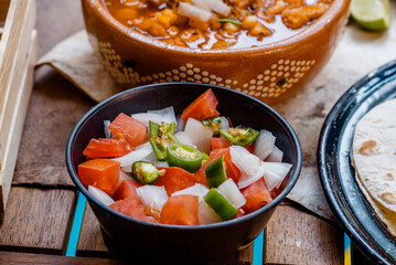 Salsa pico de gallo en una mesa rustica de madera servida con pozole y menudo