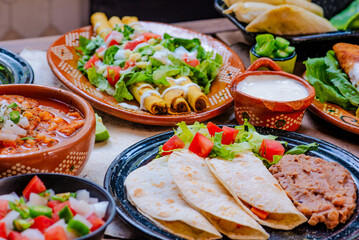Platillos de comida mexicana, Flautas de maíz, ensalada de lechuga, tomate, cebolla, crema de vaca, chile, salsa y queso, en platos de barro tradicional mexicano, en una mesa rustica de madera