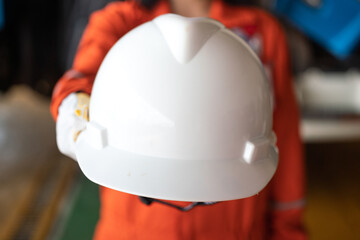 A construction worker is giving a white safety helmet or hardhat to the camera. Industrial safety...