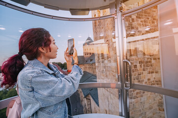 A blogger girl takes photos on her phone while riding a Ferris wheel in an amusement park in the center of the old town of Osnabruck