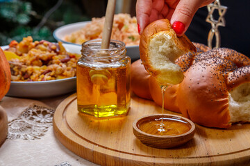 A woman's hand dips a piece of challah in honey in honor of the celebration of Rosh Hashanah nearby...