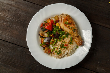 Rice with vegetables in sauce and chicken leg in a white plate on a wooden table.