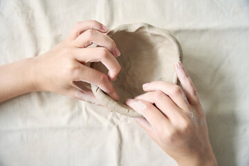 Women hands sculpt a clay bowl, top view