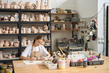 Young female student practicing in a pottery studio - obrazy, fototapety, plakaty