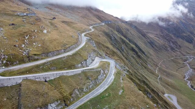 Aerial view of serpentine road of Swiss mountain pass Furka Pass with mountain panorama in the background on a cloudy late summer day. Drone video, Alps, Switzerland.