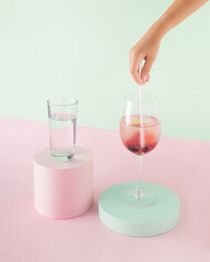 Child’s hand puts paper straw in glass of infused detox water with fresh red berries. Isolated pastel pink and green background. Minimal concept of summer party healthy beverages. Creative card.