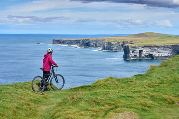 nice senior woman on mountain bike, cycling on the cliffs of Dunmore Head near Kilballyowen ,...