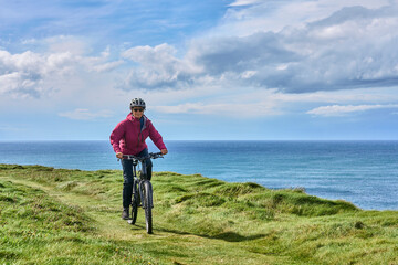 nice senior woman on mountain bike, cycling on the cliffs of Dunmore Head near Kilballyowen ,...