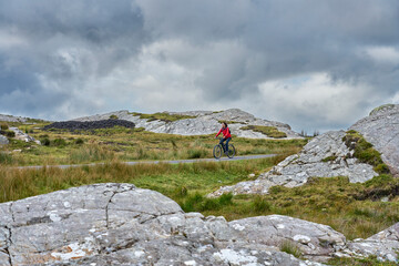 nice senior woman on mountain bike, cycling in the rough karst landscape of Burren near Ballyvaughan, County Clare in the western part of the Republic of Ireland