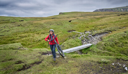 Fototapeta na wymiar nice senior woman carrying her mountain bike, on the cliffs of Malin Head, Donegal, the northern most point of Ireland