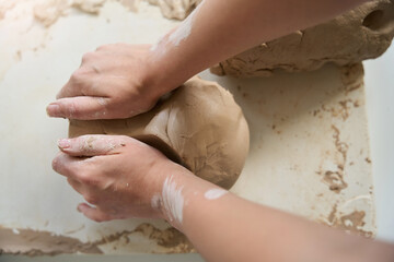Craftswoman kneads piece of clay with her hands on table