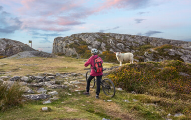 nice senior woman on mountain bike, cycling in sunset on the cliffs of Sheeps Head, County Cork, in...