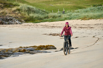 Fototapeta premium nice senior woman on mountain bike, cycling in sunset at the golden sand beach of Sillerna, Grallagh, County Galway, in the western part of the Republic of Ireland