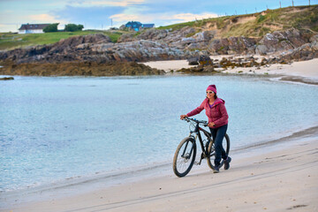 Obraz premium nice senior woman on mountain bike, cycling in sunset at the golden sand beach of Sillerna, Grallagh, County Galway, in the western part of the Republic of Ireland