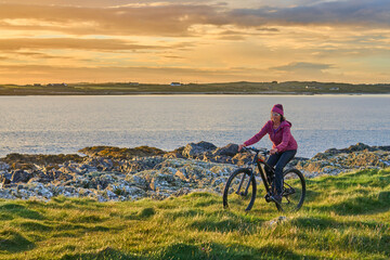 Fototapeta premium nice senior woman on mountain bike, cycling in sunset on the cliffs of Sillerna, Grallagh, County Galway, in the western part of the Republic of Ireland